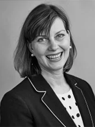 Black and white portrait of Janet Hughes, smiling confidently in professional attire with a polka-dotted blouse and a blazer.