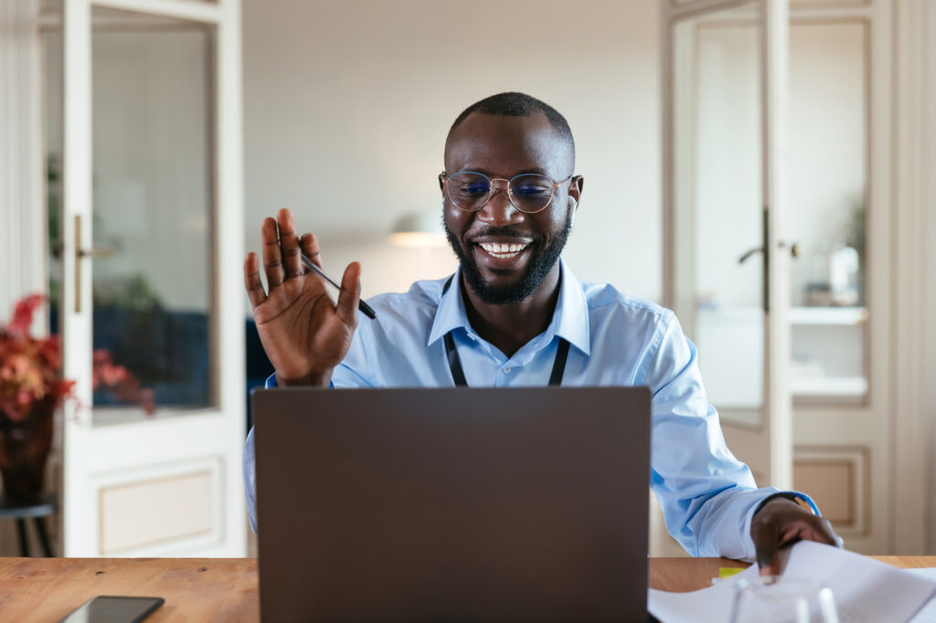 Smiling professional waving during a video call at his desk.