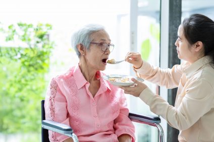 A woman is feeding an elderly woman in a wheelchair with a spoon.