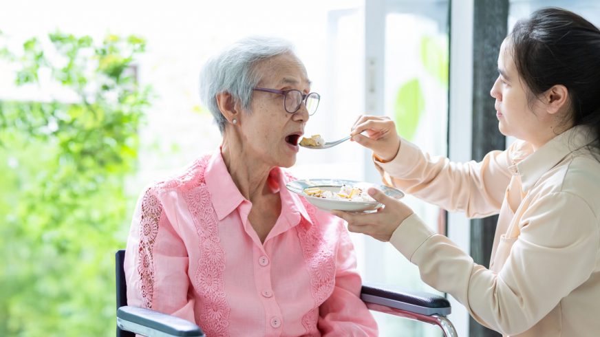 Young female caregiver or daughter feeding senior woman or mothe